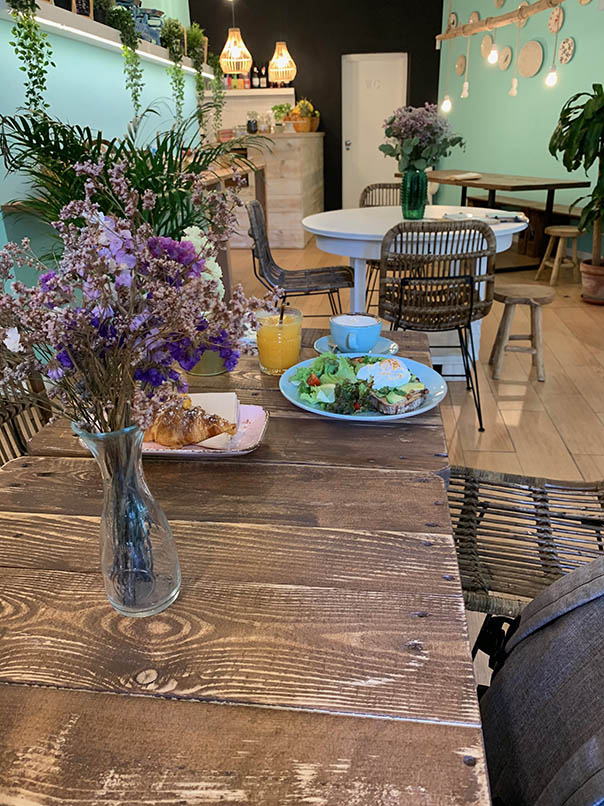 interior do café restaurante o Break Alfama móveis boémios bouquets de flores secas verde plantas parquet paredes piso verde pálido em primeiro plano um brunch servido