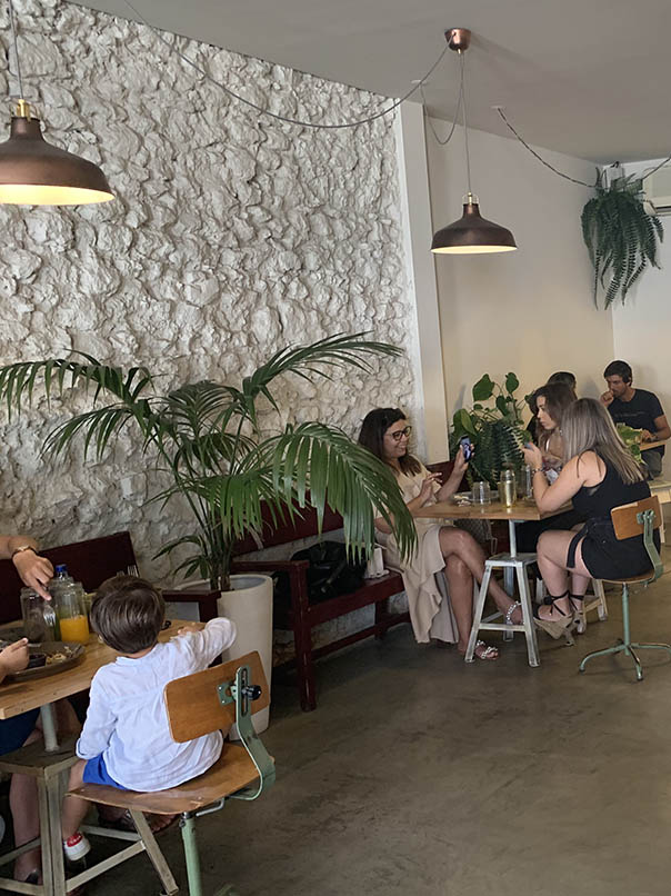 binnenland van Fauna & Flora café restaurant vintage tafel met klanten geïnstalleerd eenvoudig decor groene planten witte muren vintage tafels en stoelen
