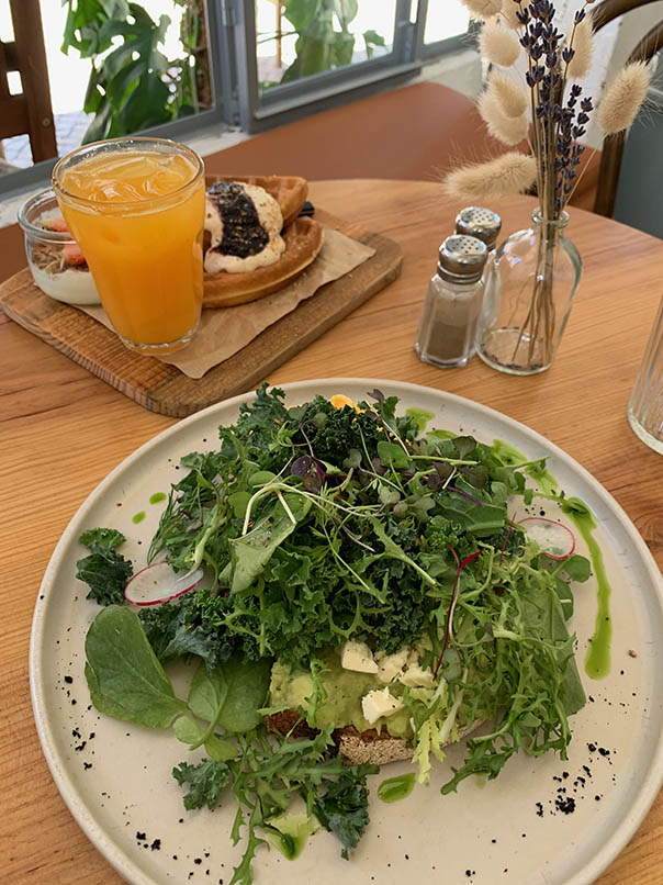interior Heim café wooden table with served dishes plate avocado toast salad baby greens and kale orange juice blueberry jam abyss  