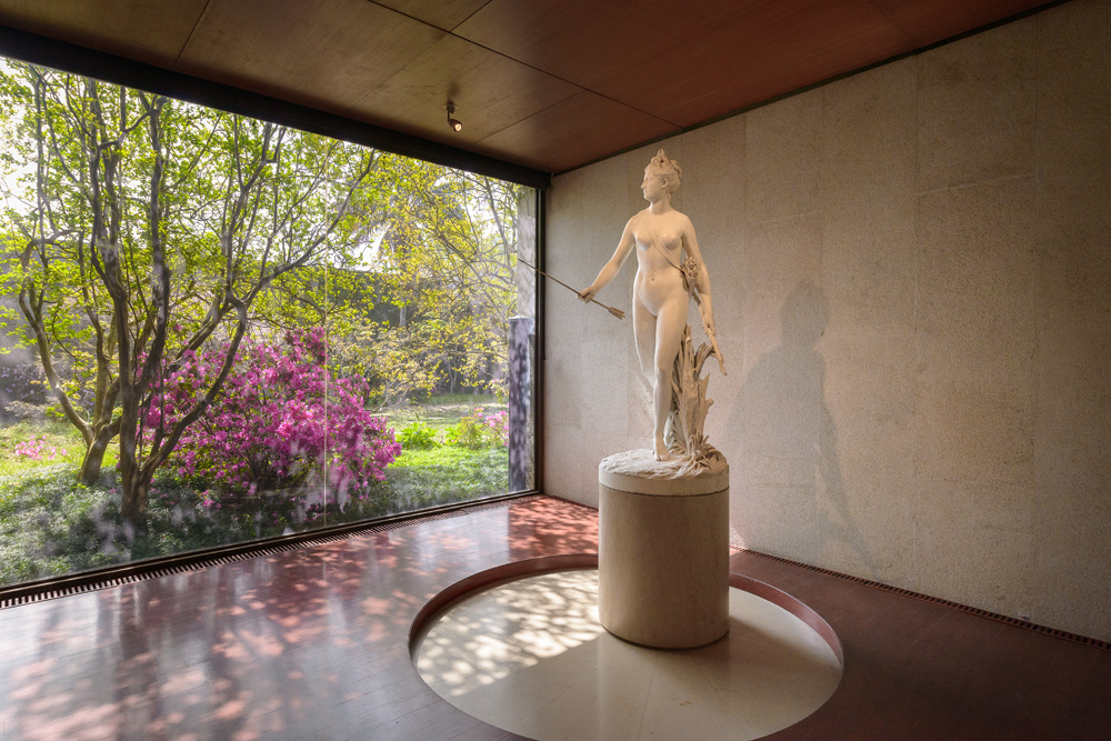 Sala del museo Calouste Gulbenkian con una estatua de la diosa romana Diana con vistas al verde y florido jardín del museo 