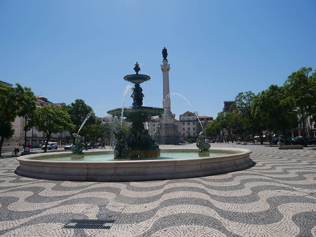 Praça do Rossio com pedras de calçada pretas e brancas em ondas com sua fonte e estátua de Pedro IV, Rei de Portugal